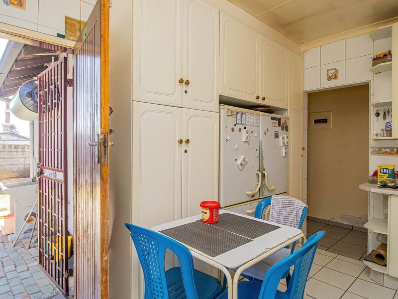 A dated kitchen featuring built-in cabinetry, tiled flooring, and a direct access point to an outdoor patio area through a security gate.