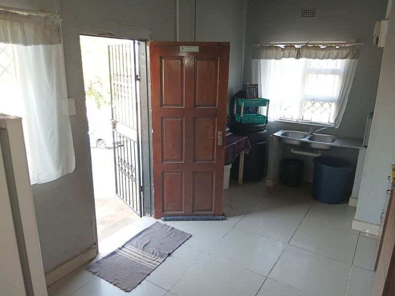 A functional kitchen area featuring tiled flooring, a double bowl stainless steel sink, and direct access to the exterior via a timber door.