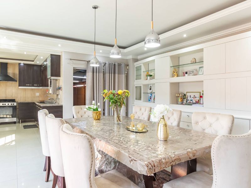 Open plan dining area featuring built-in display cabinetry, elegant pendant lighting, and seamless flow into a modern kitchen with gas stove and extractor.