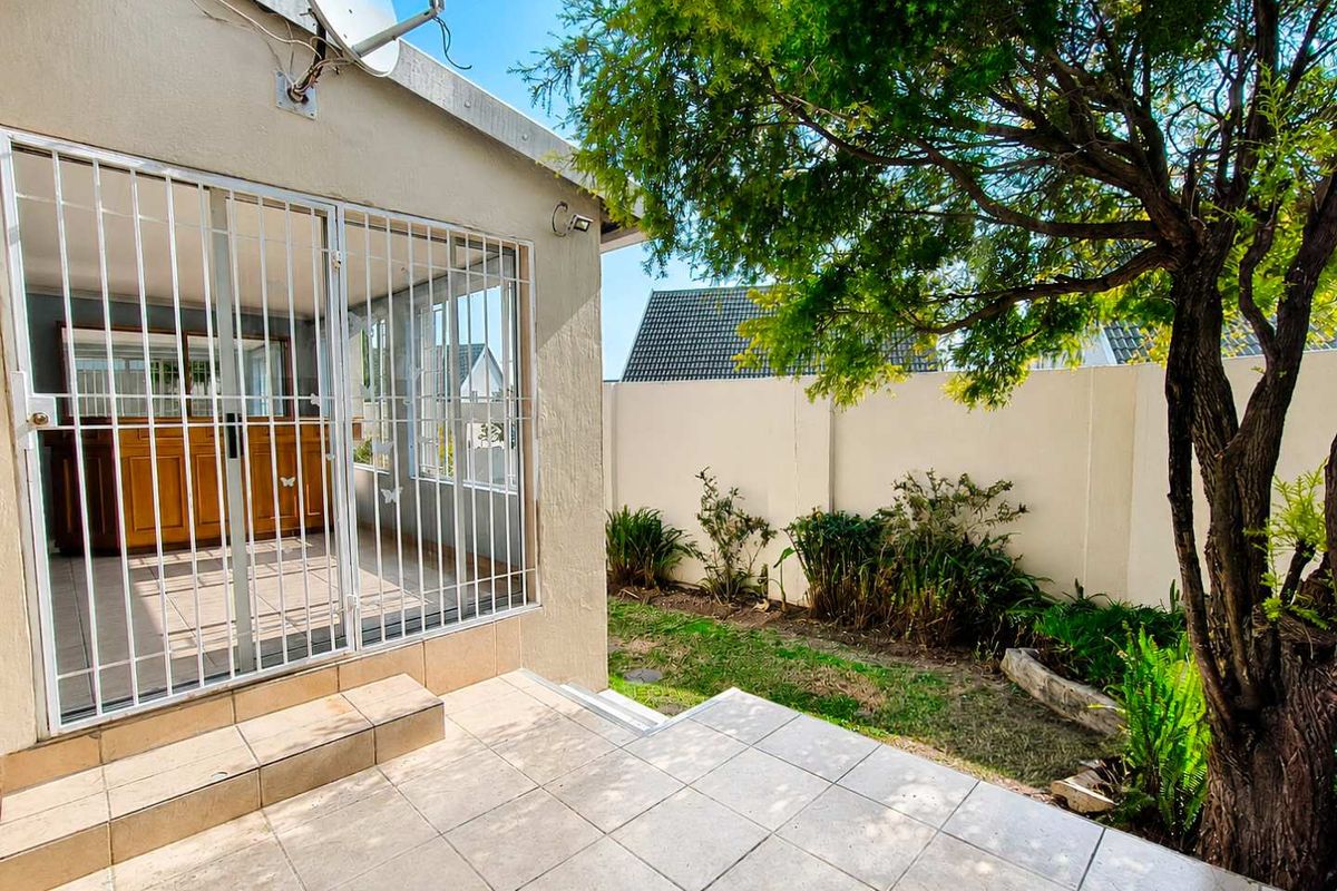 A private rear patio area featuring tiled flooring, a security gate, and a small garden space enclosed by a boundary wall.