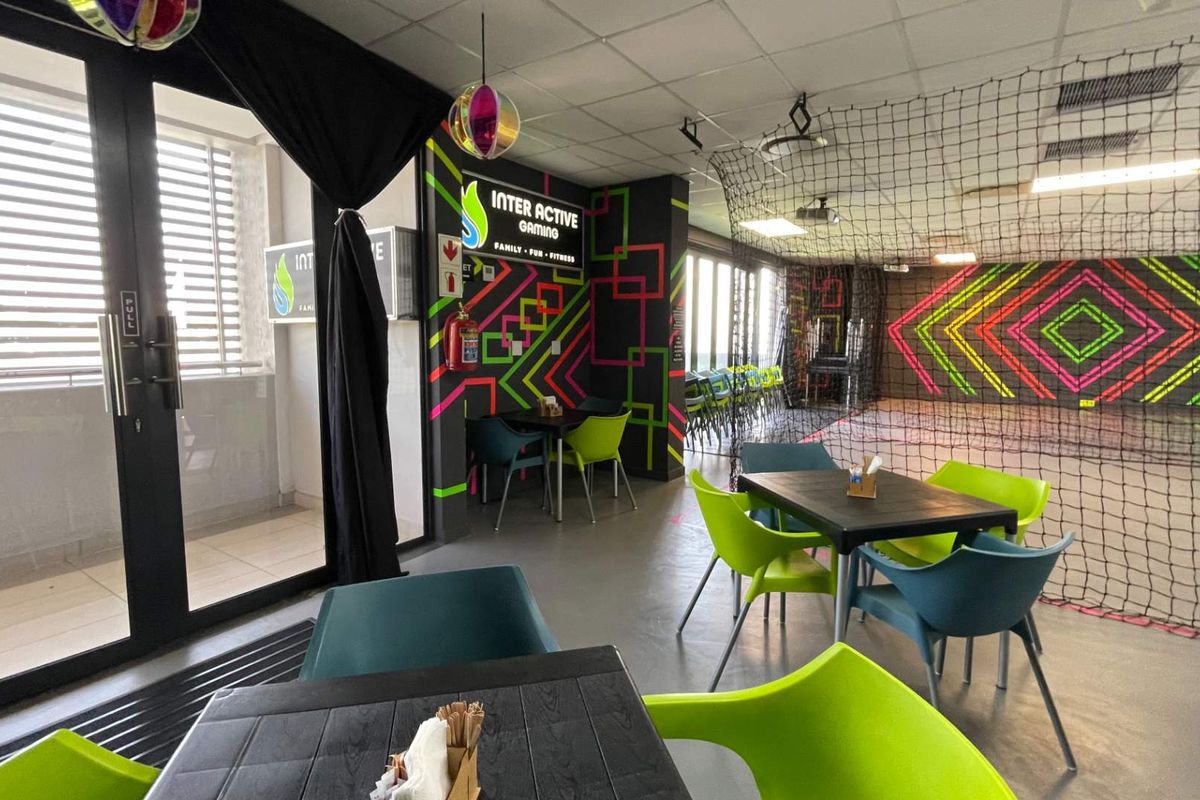 A vibrant, multi-purpose recreational space featuring modern lighting, safety netting, and direct access to an outdoor balcony area.