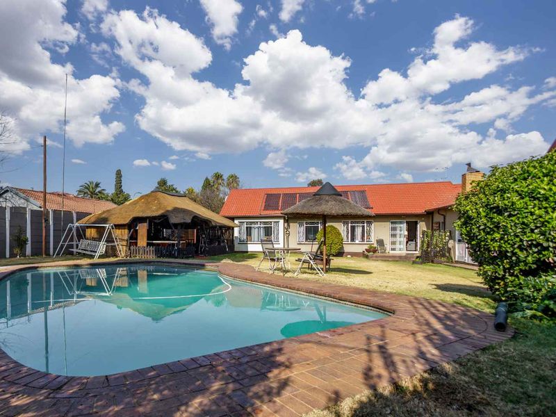 Rear exterior view of the cottage featuring a swimming pool, a thatched lapa, and solar water heating panels on the tiled roof.