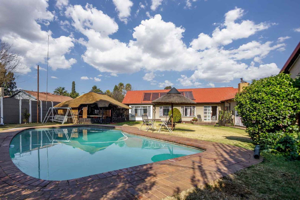 Rear exterior view of the cottage featuring a swimming pool, a thatched lapa, and solar water heating panels on the tiled roof.