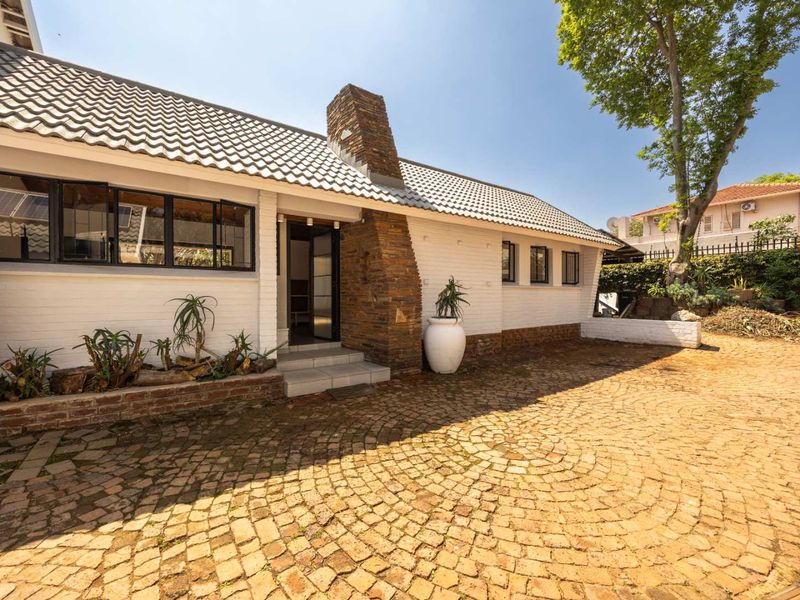 Rear exterior view featuring a distinctive stone-clad chimney, tiled roof, and extensive cobblestone paving leading to the home entrance.