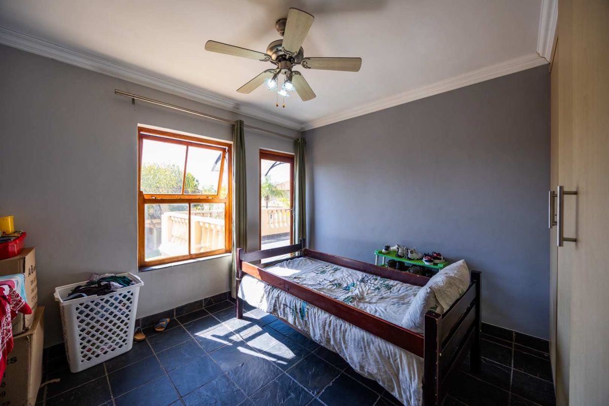 A bedroom featuring tiled flooring, a ceiling fan, and built-in cupboard storage, with natural light entering through a wooden-framed window.