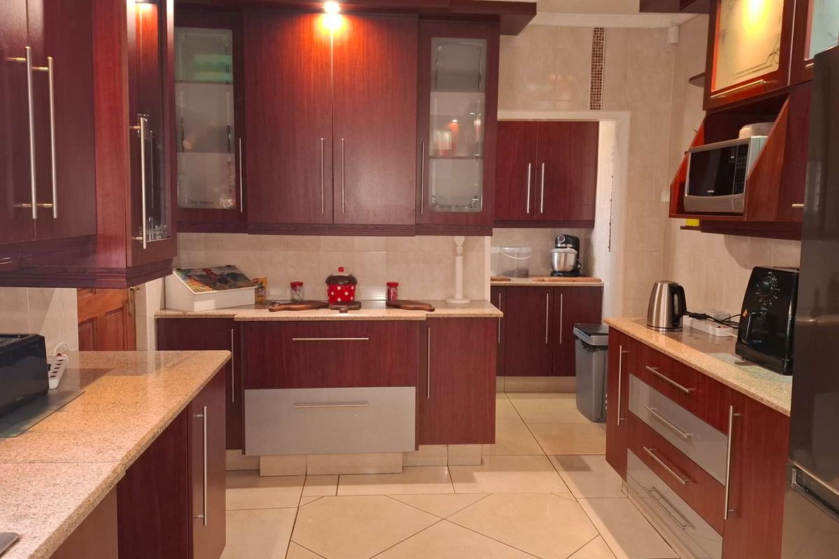 A functional kitchen featuring dark wood cabinetry, granite countertops, tiled flooring, and a separate scullery area for additional storage and preparation space.