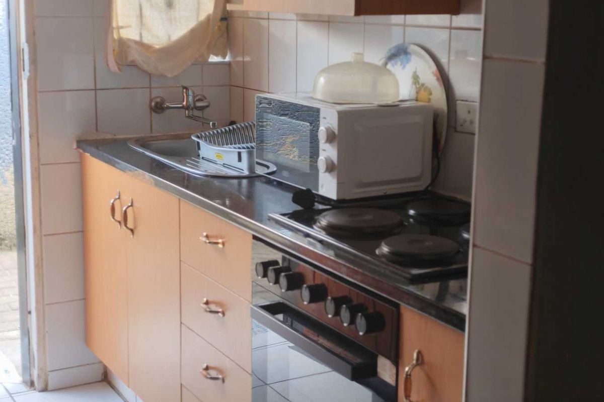 Compact kitchen featuring built-in cabinetry, electric hob, oven, and tiled splashback. The space offers functional storage and preparation areas with a dated aesthetic.