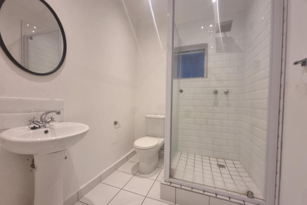 A clean, modern bathroom featuring a pedestal basin, a white toilet, and a glass-enclosed shower with subway tile finishes.