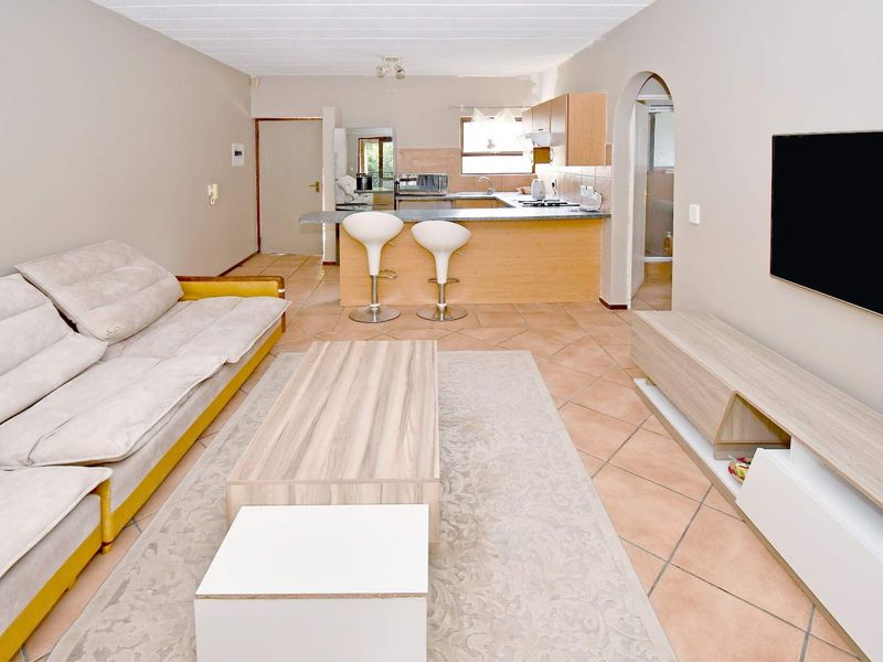 Open-plan living area featuring a functional kitchen with built-in cabinetry, breakfast counter, and tiled flooring throughout the combined space.