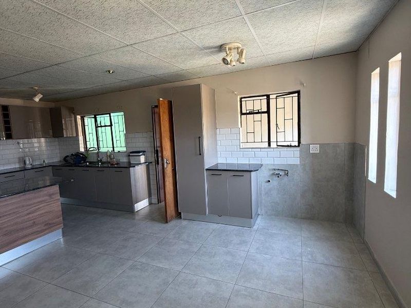 Spacious kitchen featuring modern grey cabinetry, granite countertops, subway tile backsplash, and tiled flooring, offering a functional layout with plumbing for appliances.