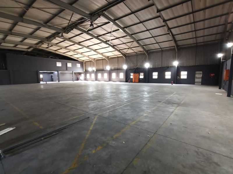 Spacious industrial warehouse featuring high ceilings, concrete flooring, and integrated high bay lighting, suitable for storage or manufacturing operations.