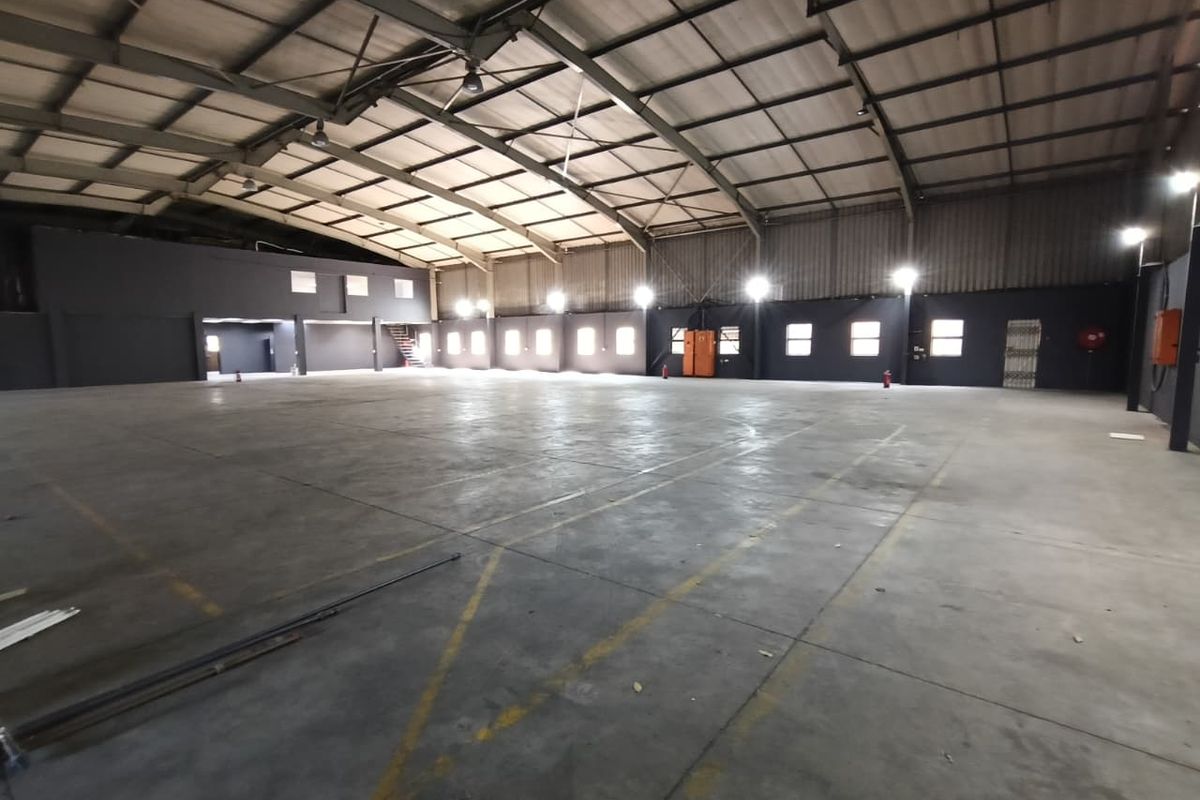Spacious industrial warehouse featuring high ceilings, concrete flooring, and integrated high bay lighting, suitable for storage or manufacturing operations.