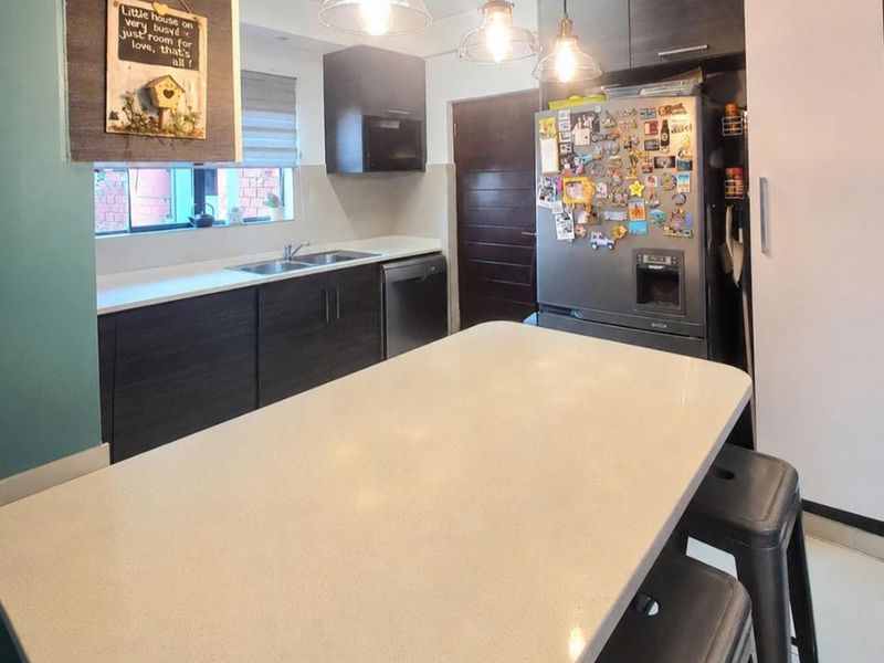 Modern kitchen featuring a large quartz-topped island, dark cabinetry, integrated appliances, and stylish pendant lighting, creating a functional and contemporary cooking space.