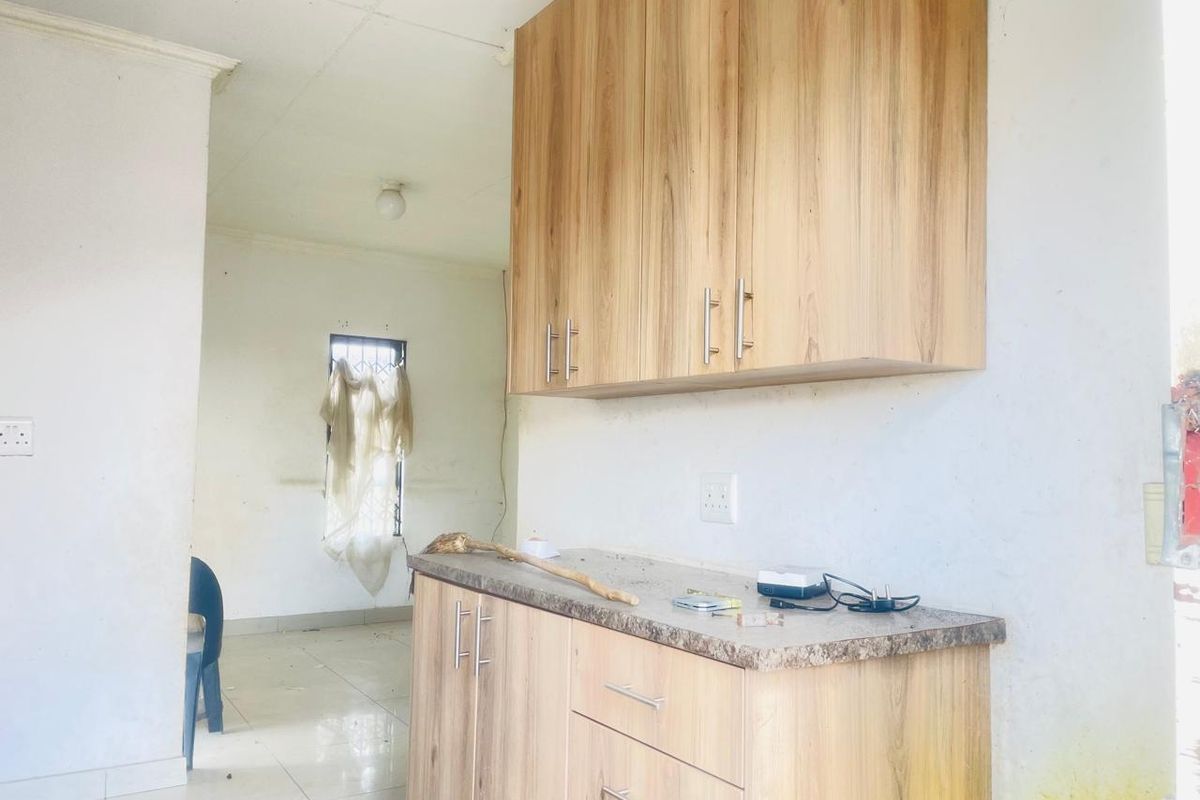 A small kitchen area featuring light wood-look cabinetry, laminate countertops, and tiled flooring, requiring some cosmetic updates and maintenance.