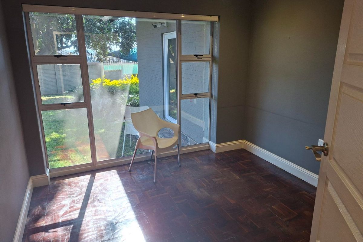 A bright, empty bedroom featuring classic parquet flooring and a large window providing natural light and garden views.