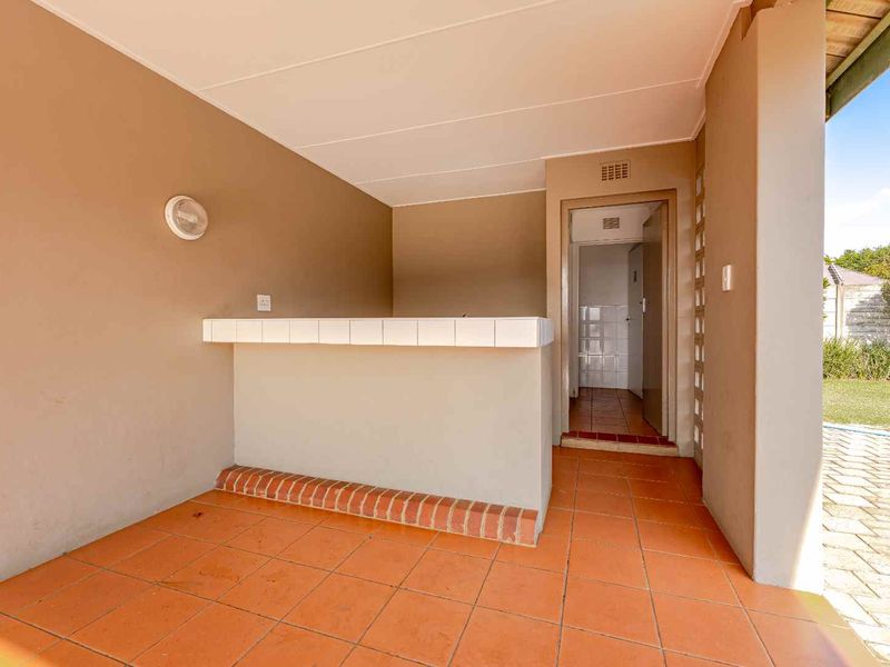 A covered outdoor patio area featuring a built-in bar counter and tiled flooring, providing a functional space for outdoor entertaining.