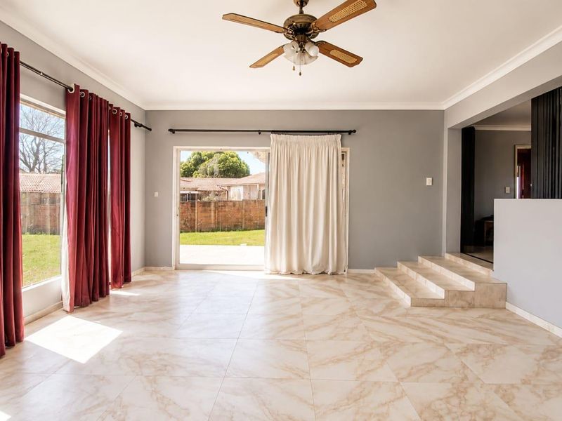 Spacious, light-filled living room featuring neutral tiled flooring, a ceiling fan, and large sliding glass doors providing direct access to the rear garden.