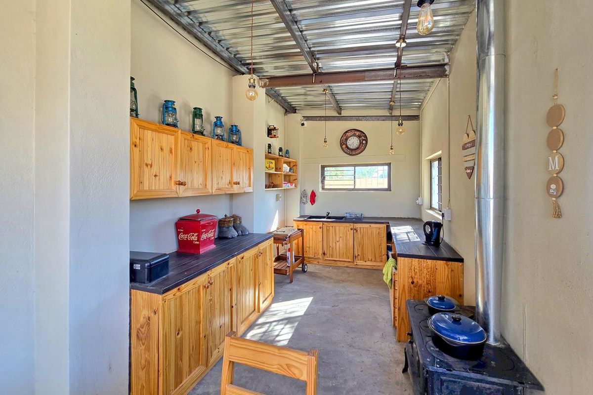 A rustic kitchen area featuring wooden cabinetry, a built-in wood-burning stove, and an industrial-style exposed ceiling structure.