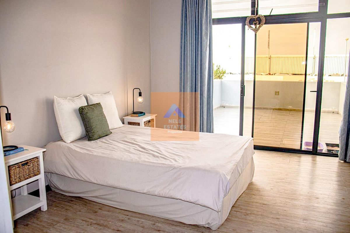 A bright bedroom featuring laminate flooring and large sliding glass doors that provide direct access to an outdoor balcony area.