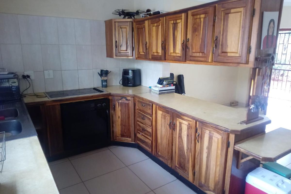 A functional kitchen featuring solid wood cabinetry, a built-in electric hob, tiled splashbacks, and tiled flooring with a breakfast counter extension.