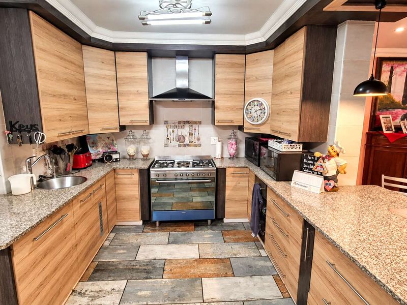 A well-maintained kitchen featuring wood-finish cabinetry, granite countertops, a stainless steel gas stove with extractor fan, and durable tiled flooring.