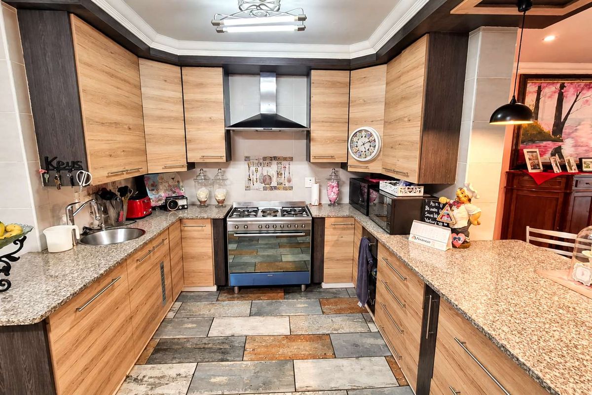 A well-maintained kitchen featuring wood-finish cabinetry, granite countertops, a stainless steel gas stove with extractor fan, and durable tiled flooring.