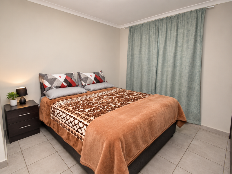 A well-maintained bedroom featuring neutral wall tones, tiled flooring, and a built-in wardrobe with modern finishes.