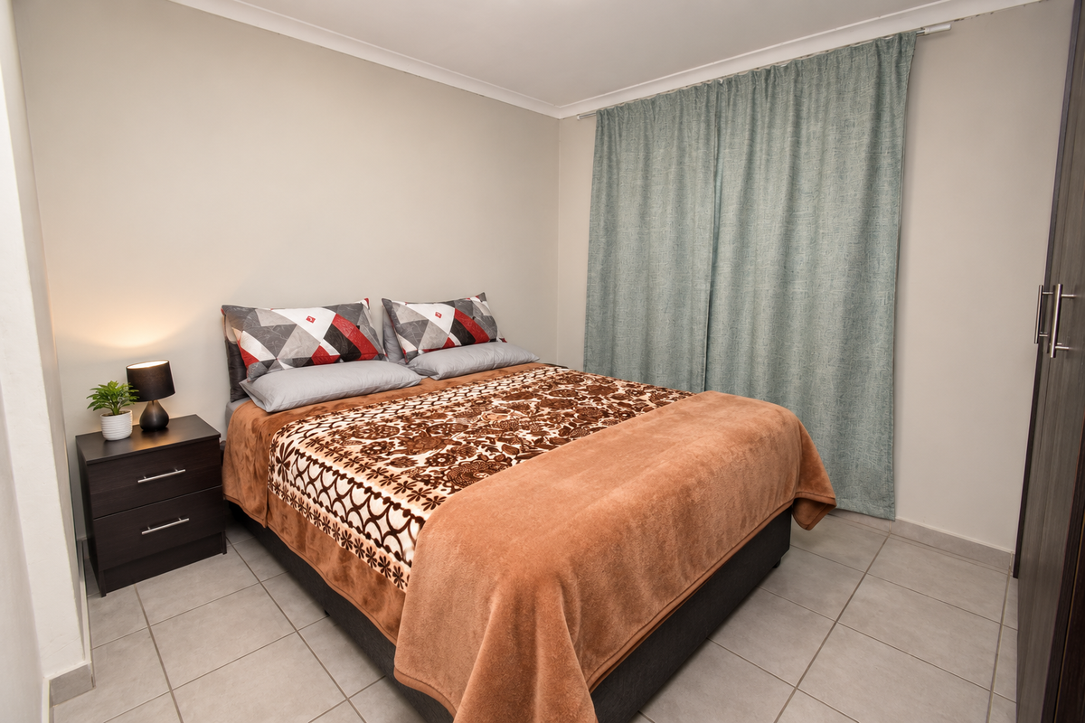 A well-maintained bedroom featuring neutral wall tones, tiled flooring, and a built-in wardrobe with modern finishes.