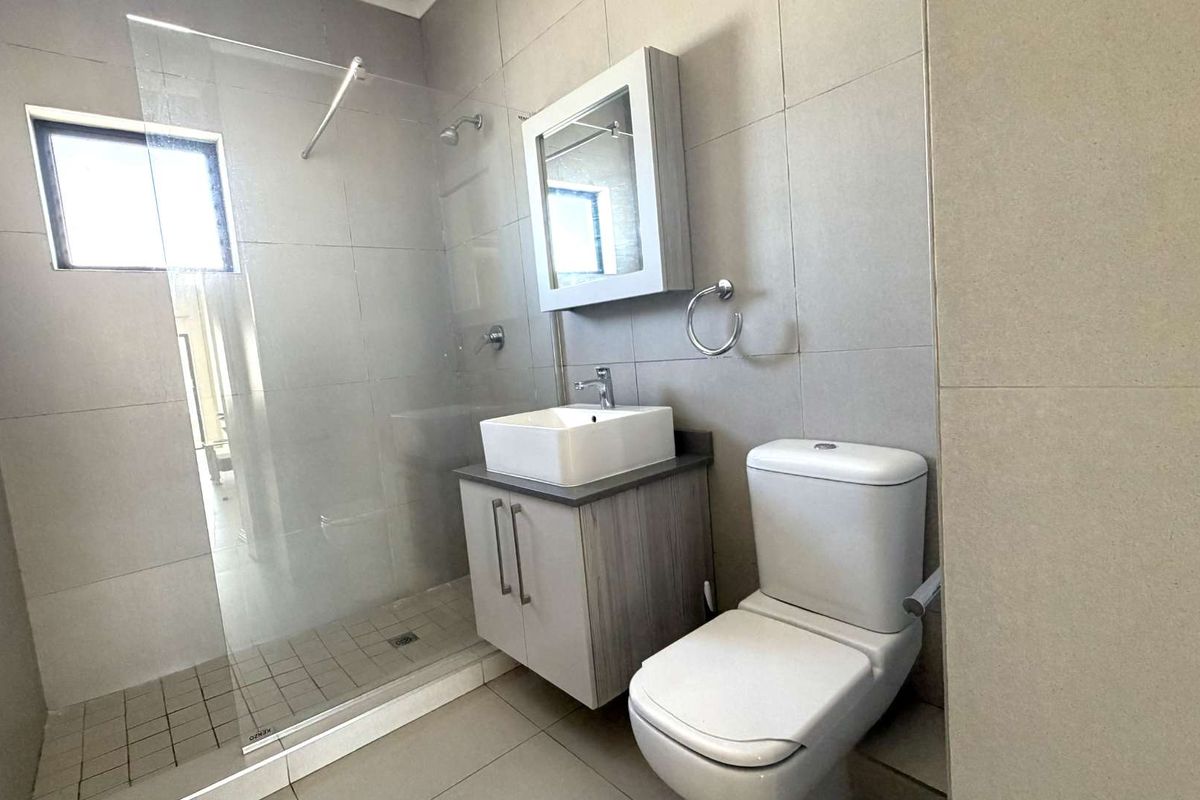 Modern bathroom featuring a glass-enclosed walk-in shower, a contemporary vessel sink vanity, and a white ceramic toilet with neutral wall and floor tiling.