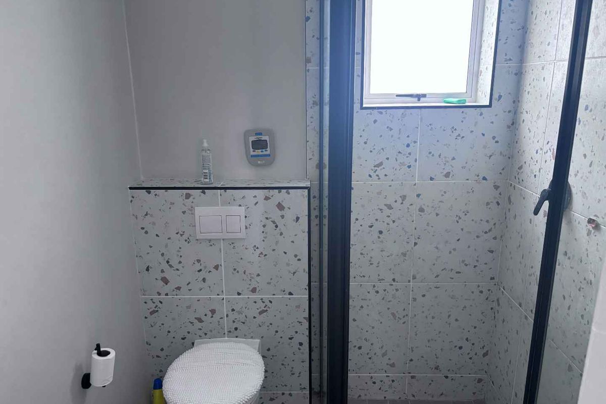 A modern bathroom featuring a wall-mounted toilet with a concealed cistern and a glass-enclosed shower with terrazzo-style wall tiling.