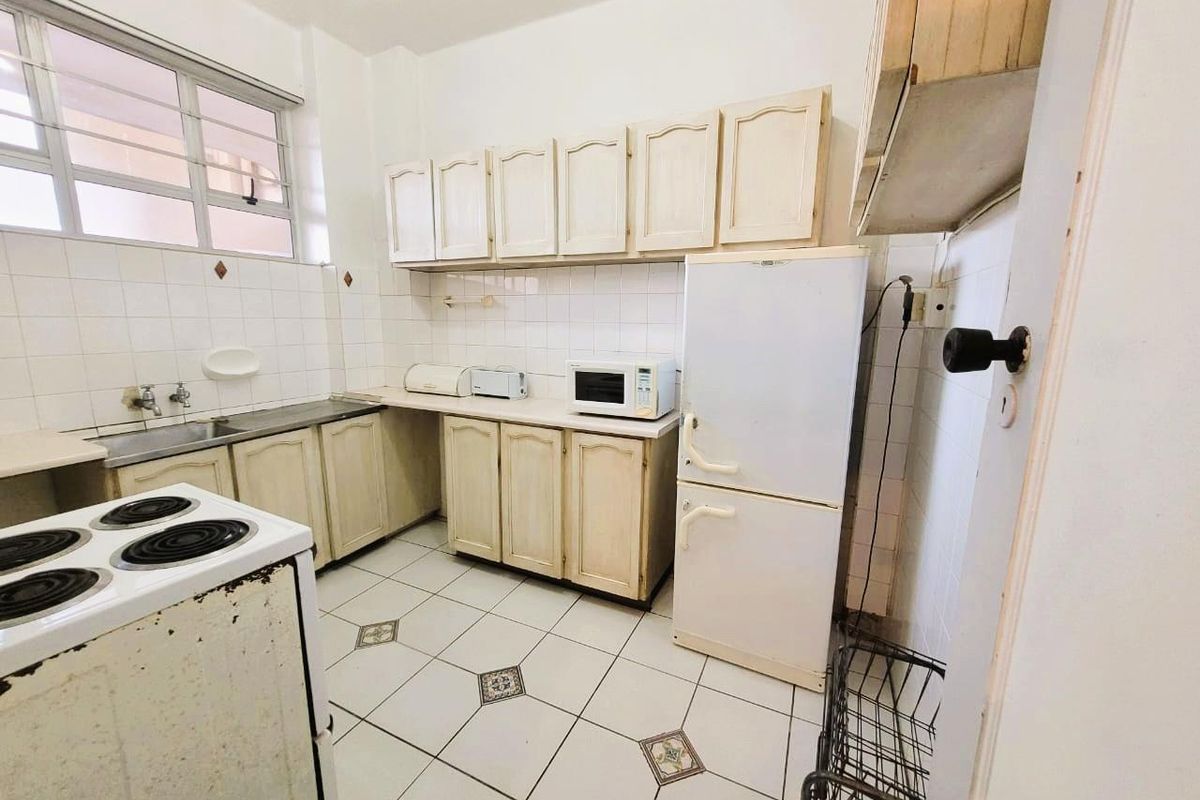 A dated kitchen featuring traditional cabinetry, tiled backsplash, and ceramic floor tiles, offering a functional layout ready for modernization.