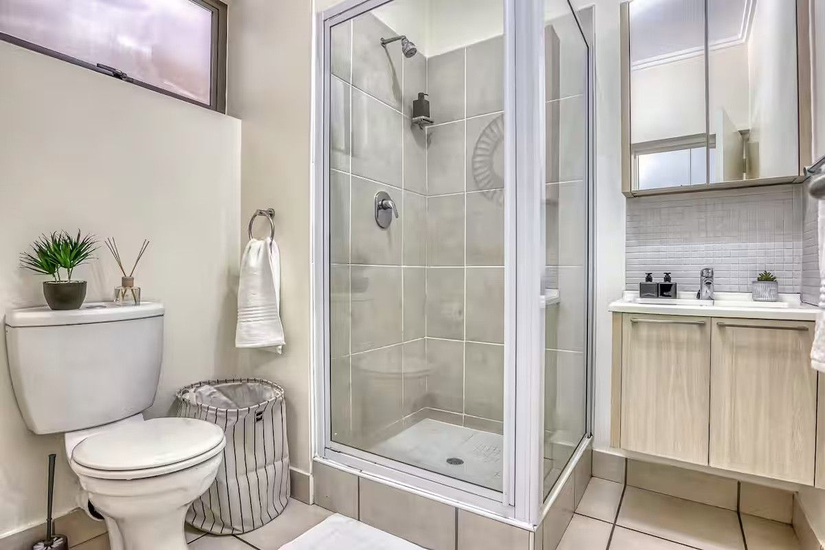 A compact, well-maintained bathroom featuring a glass-enclosed shower, a modern vanity with integrated basin, mirrored storage, and a standard toilet.