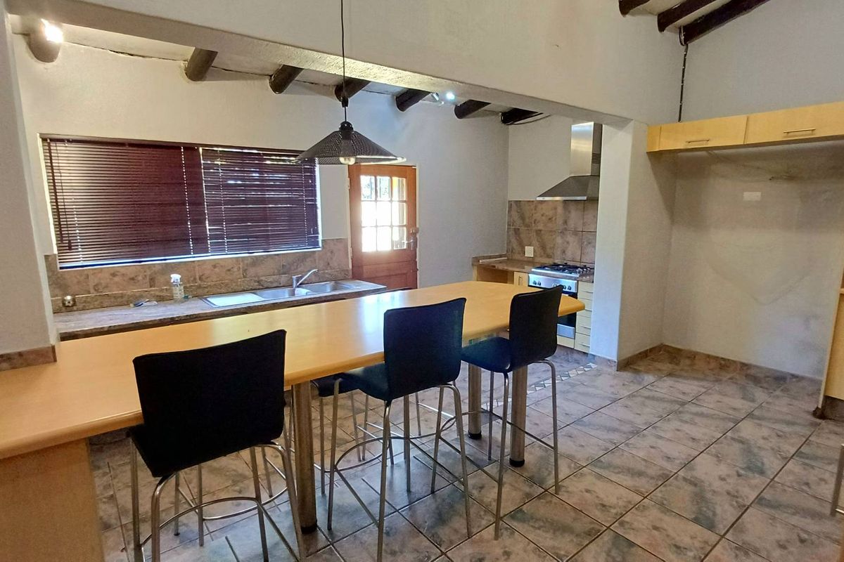 Open-plan kitchen featuring a central island, built-in cabinetry, gas hob with extractor, and exposed timber ceiling beams.