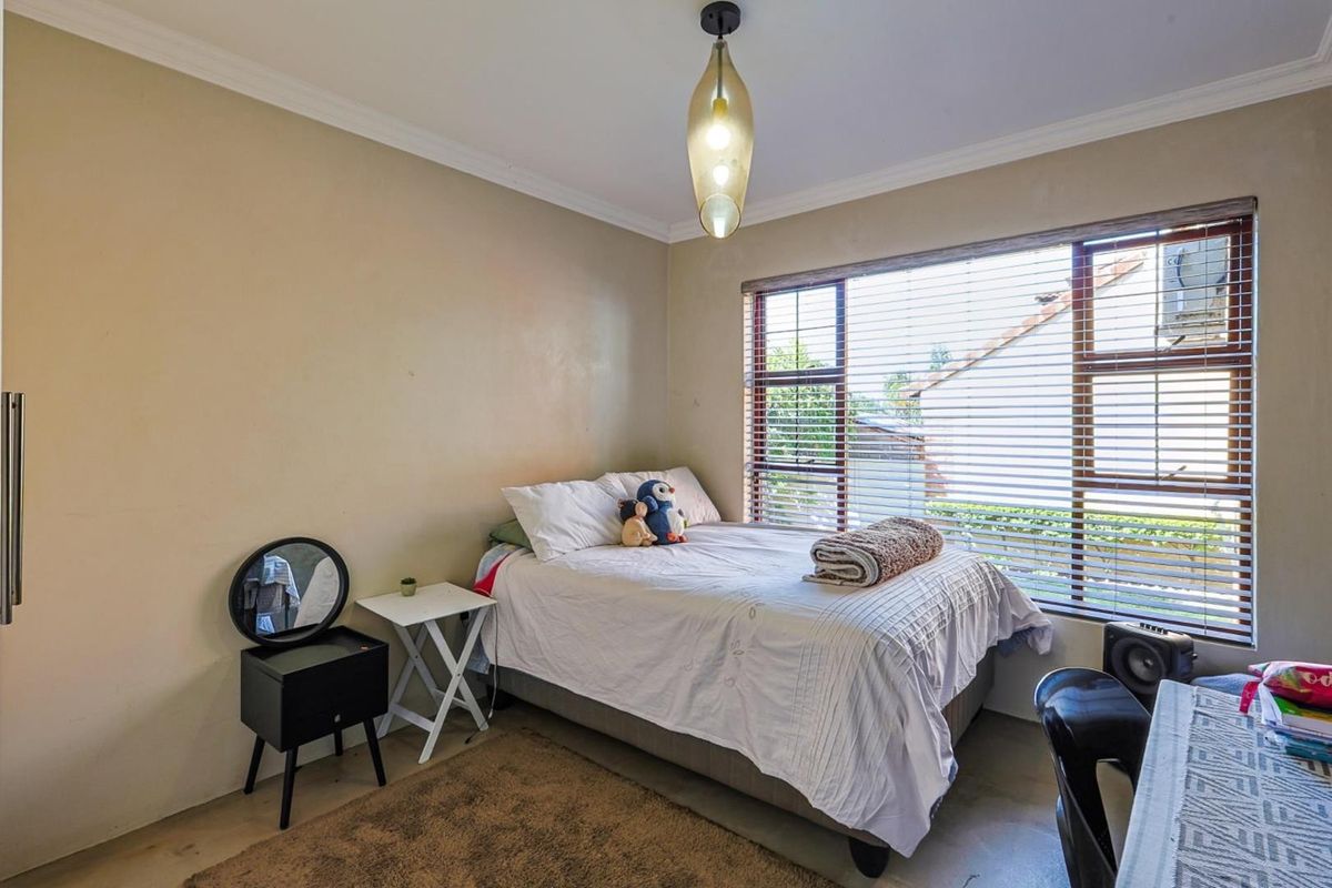 A functional bedroom featuring large windows with fitted blinds, crown molding, and a central pendant light fixture.