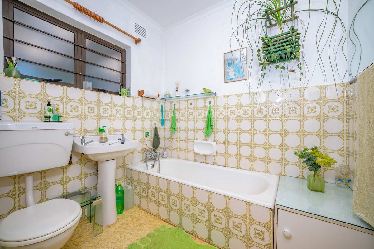 A functional bathroom featuring a pedestal basin, bathtub, toilet, and classic patterned wall tiles, offering a dated but well-maintained space.