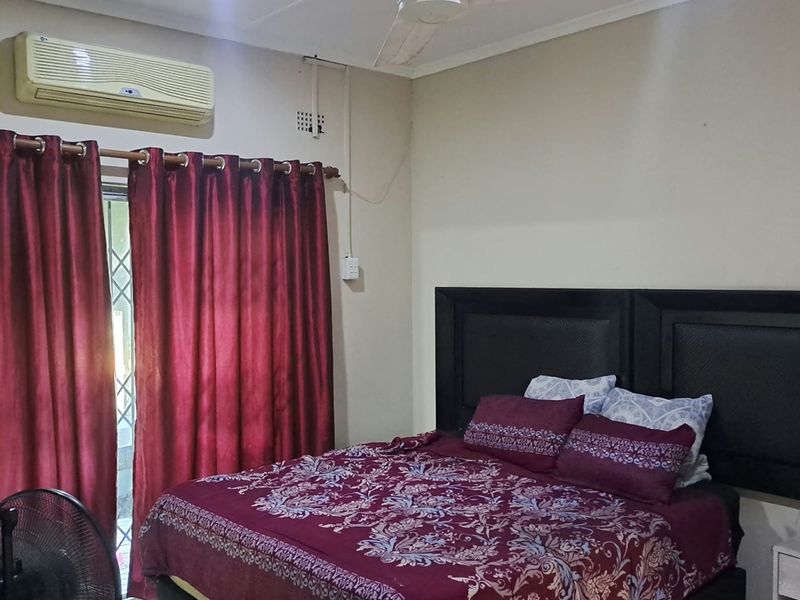 A functional bedroom featuring tiled flooring, a ceiling fan, and a wall-mounted split-system air conditioner with direct access to an outdoor area.