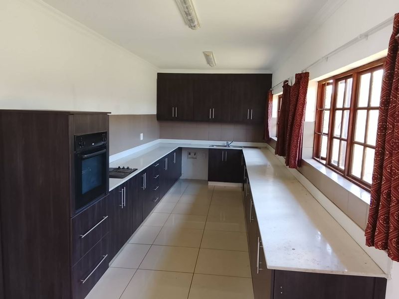 A spacious kitchen featuring dark wood cabinetry, stone countertops, built-in oven, hob, and tiled flooring, offering a clean and functional layout.