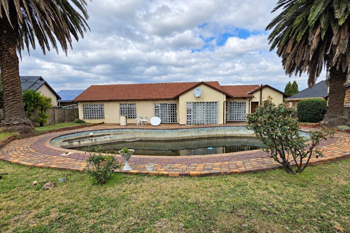 Rear view of the property featuring a large swimming pool with brick paving and established palm trees in the garden.