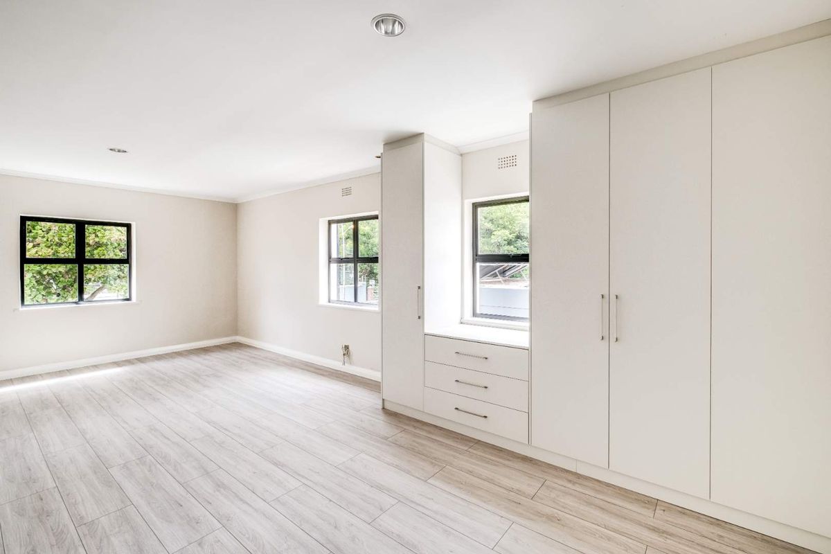A bright, spacious bedroom featuring modern light wood-look flooring, neutral walls, and extensive built-in cabinetry with integrated drawers and storage.