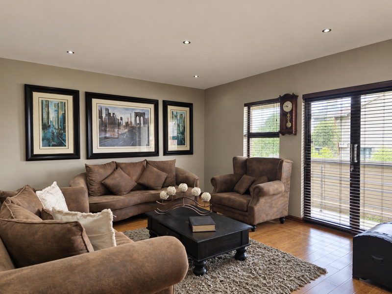 A well-maintained living room featuring hardwood flooring, recessed downlighting, and sliding glass doors with venetian blinds providing access to an outdoor area.
