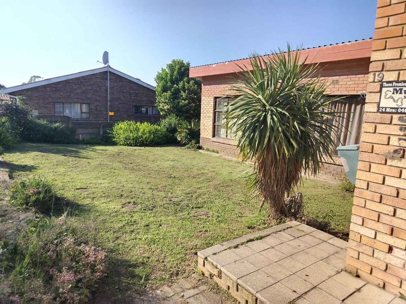 A view of the rear garden featuring a lawn area, brick exterior walls, and a small paved patio section.