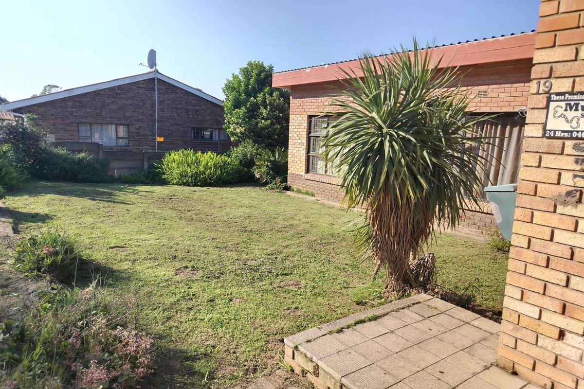 A view of the rear garden featuring a lawn area, brick exterior walls, and a small paved patio section.