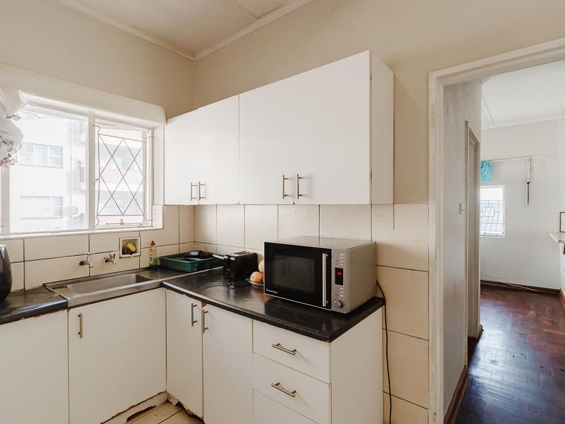 A compact kitchen featuring white built-in cabinetry, a dark laminate countertop, and a stainless steel sink with a tiled backsplash.