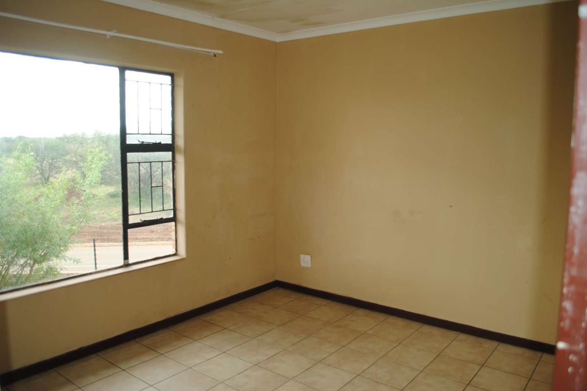 An empty bedroom featuring tiled flooring, a large window with security bars, and neutral wall finishes, requiring minor cosmetic updates.