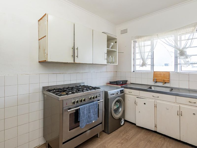 A functional kitchen featuring a gas stove, stainless steel sink, and built-in cabinetry with a tiled backsplash and laminate flooring.
