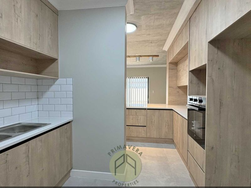 Modern kitchen featuring light wood-grain cabinetry, stone countertops, subway tile backsplash, and integrated oven, offering a clean and contemporary aesthetic.