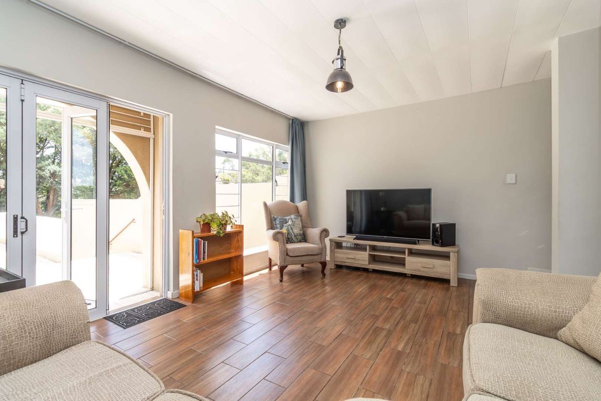 A bright living room featuring wood-look tile flooring, a modern pendant light, and large glass sliding doors providing access to an outdoor patio area.
