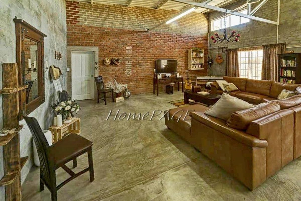 Spacious industrial-style living area featuring exposed brick walls, polished concrete flooring, and high vaulted ceilings with exposed steel trusses.