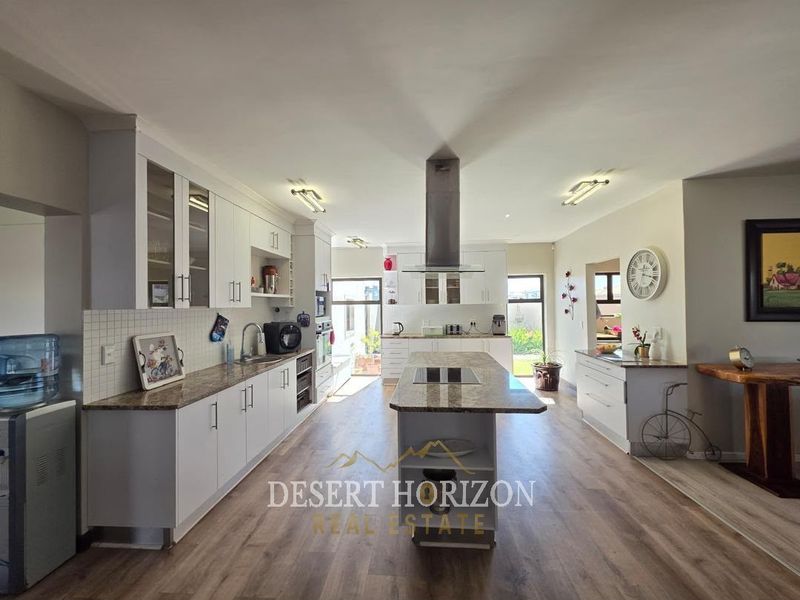 Spacious modern kitchen featuring a central island with cooktop, granite countertops, ample white cabinetry, and integrated appliances, finished with durable laminate flooring.