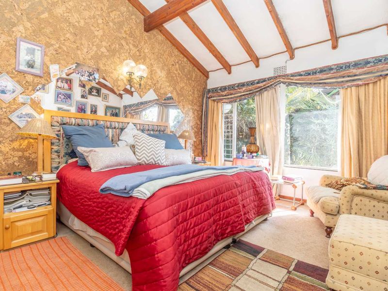 Spacious bedroom featuring exposed timber ceiling beams, unique cork wall paneling, and large windows providing natural light and garden views.